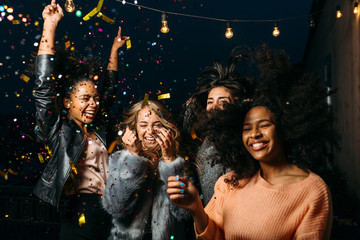 Group of female friends enjoying night party, throwing confetti - obrazy, fototapety, plakaty