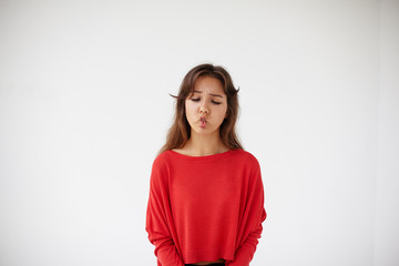 Portrait of funny beautiful young mixed race female with long dark hair making faces, pursuing lips, squinting eyes and sucking in cheeks while having fun indoors, entertaining herself. Body language