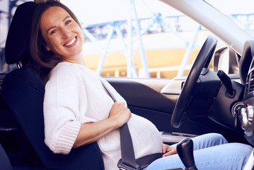 Joyful pregnant woman posing on driver seat in car