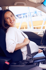 Young pregnant woman with fasten seat belt driving her car