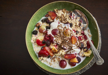 A green bowl of Muesli with mixed, chopped fruit, yogurt and seeds
