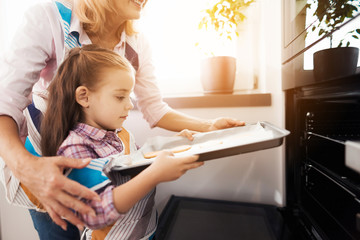 The girl loads the biscuits in the oven. Her grandmother helps her