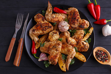 Grilled chicken wings on black plate decorated with garlic, lemon slices and chili peppers. Cooking concept, meat dishes, homemade food