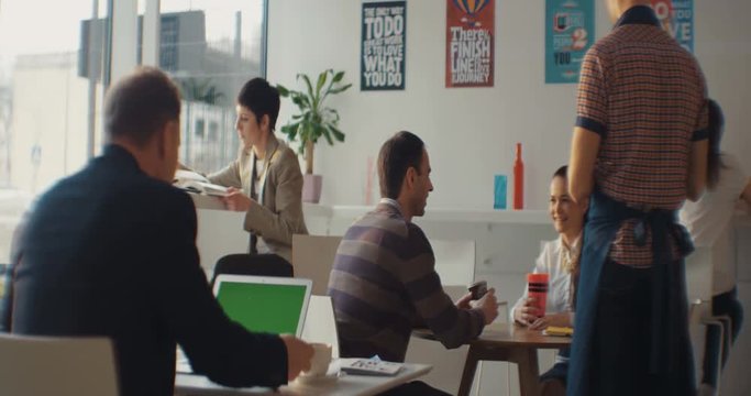 A man sitting in a cafe uses a laptop with a green screen. Around the people. The waiter accepts the order. Shot on RED Epic Camera.