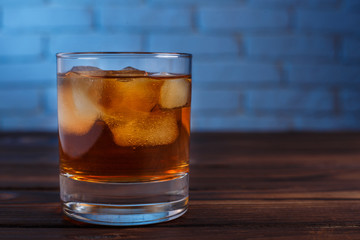 Whiskey with ice cubes on wooden table on brick wall background, copy space. Alcohol drinks, bar concept