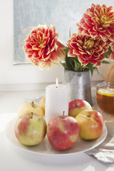 the Autumn still life with red dahlias in a tin jar, pumpkin, a cup of tea and apples on the window in sunny weather