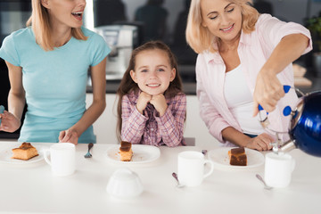 Two women and a girl getting ready to drink tea with a homemade pie in their kitchen