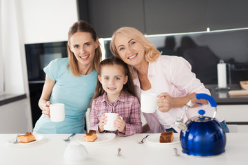 Family posing in the kitchen with cups of tea in hands. They look at the camera and smile.
