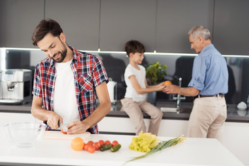 Prepare a salad for Thanksgiving with the whole family. A man, his father and son prepare a salad in the kitchen