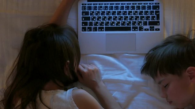 Children play on the computer in the bed under the blanket at night. Children fell asleep near the computer. Computer games.