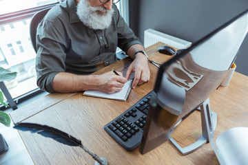 Concentrated elderly man is noting his ideas