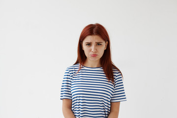 Horizontal studio portrait of upset sad Caucasian teenage girl with red colored hair and pursed lips having disappointed unhappy look, frowning and pouting after quarrel or fight with her boyfriend