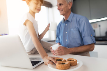 The old man and the boy are drinking tea in the kitchen. The boy is drawn to the cake