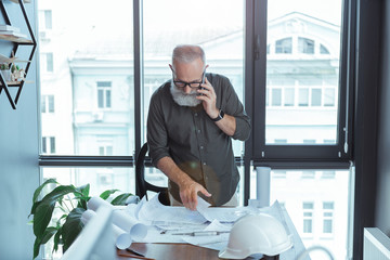 Skillful old architect is having conversation on smartphone