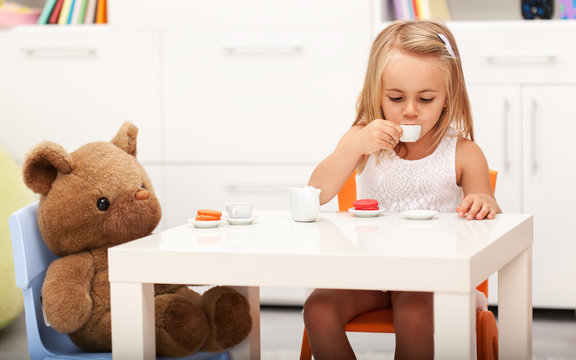 Little girl having some tea with her toy bear