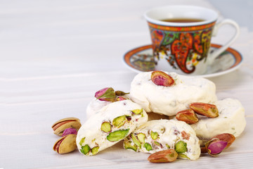 Traditional Iranian and Persian pieces of white nougat dessert sweet candies (Gaz) with Pistachio nuts from Isfahan City and a cup of tea on white wooden background