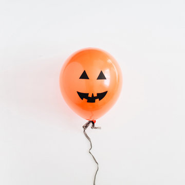 Halloween minimal concept. One orange balloon with funny smiling face on white background. Flat lay, top view.