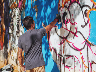Fototapeta na wymiar Creative art - teenage boy painting colorful abstract ornament graffiti on street wall with aerosol spray. Back view, overall plan