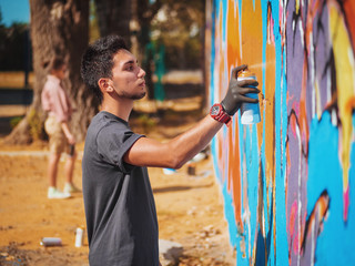 Handsome Talented Young Boy making a colorful graffiti with aerosol spray on urban street wall. Cinematic tonedshot. Creative art. Side view