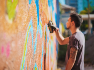 Handsome Talented Young Boy making a colorful graffiti with aerosol spray on urban street wall....
