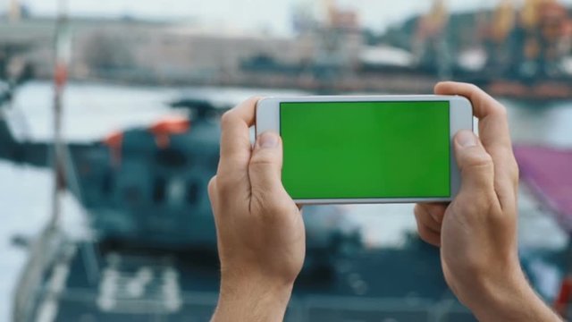 Closeup young male man hands holding modern white smartphone mobile green touch screen chromakey blurred helicopter background horizontal outside taking picture online media digital device development