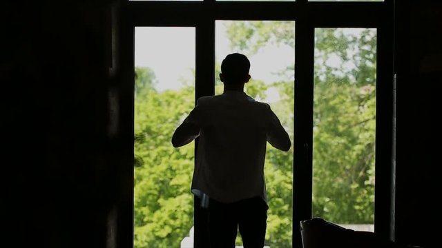 Man putting on shirt standing by window at home, slow motion