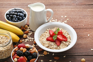 Oat flakes in plate with berries, nuts and milk on wooden table