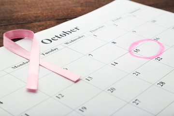 Pink ribbon with calendar sheet on wooden table