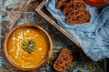 Bowl of traditional homemade pumpkin soup with seads, cream and bread on rustic wooden table
