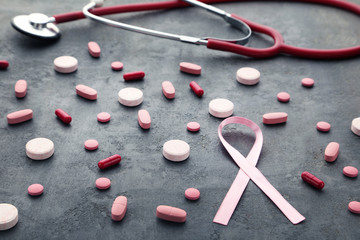 Pink ribbons with tablets and capsules on grey wooden table