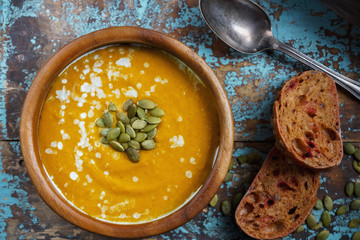 Bowl of traditional homemade pumpkin soup with seads, cream and bread on rustic wooden table