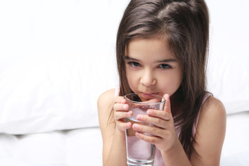 Beautiful little girl drinking water on white bed