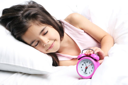 Beautiful little girl sleeping with alarm clock in white bed