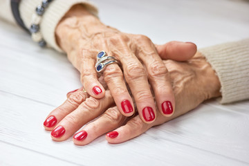 Woman manicured hands on table. Female aged hands with perfect red nails and silver luxury ring.