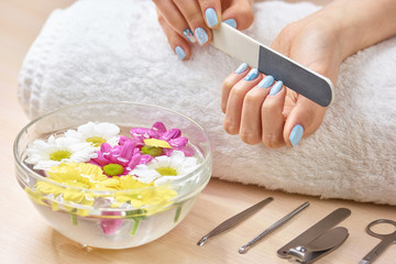 Obraz na płótnie Canvas Woman filling nails on towel. Young woman hands in spa salon polishing manicured nails, bath for hands, manicure equipment.