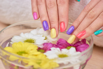 Obraz na płótnie Canvas Female hands receiving spa treatment. Young woman beautiful hands with summer colorful nails in bath with aroma water and flowers.