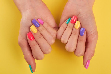 Fototapeta premium Female nails varnished in different colors. Womans nails covered with multicolor polish on yellow background, top view.