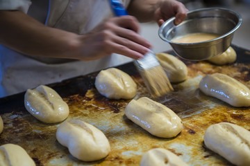 Trabajador en una panadería pintando con huevo los bollos y piezas antes de hornearlos
