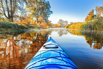 View from the blue kayak on the river banks with autumnal yellow leaves trees in fall season. The...