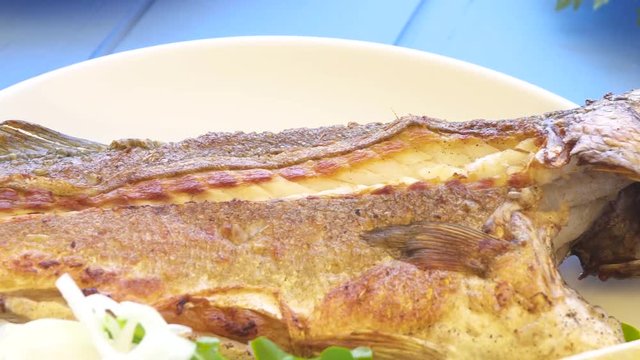 Grilled sea bass on plate with onions, sliced lemon and garden rocket aragula on blue table. Greek food.