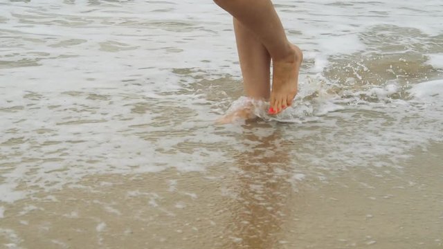 The legs of a woman walking on the waves. Feet in the waves of the sea.