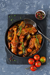 Chicken stewed with vegetables and tomato on a stone board in a frying pan.