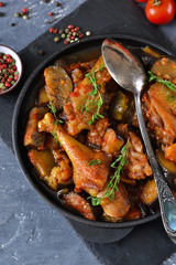 Chicken stewed with vegetables and tomato on a stone board in a frying pan.