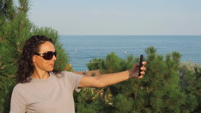The girl takes pictures of herself against the background of the sea. Young woman on a background of a sea landscape with a phone.