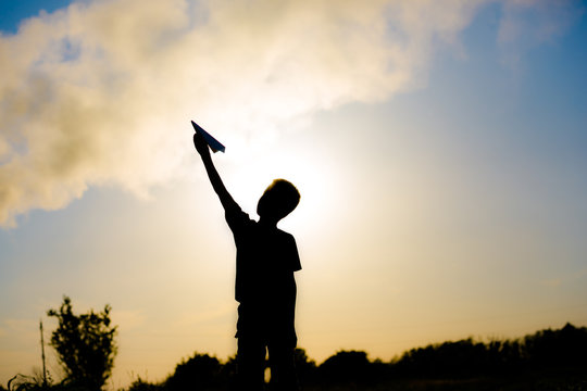 A happy child is playing with a paper airplane at sunset. Classes with children outdoors. Lifestyle