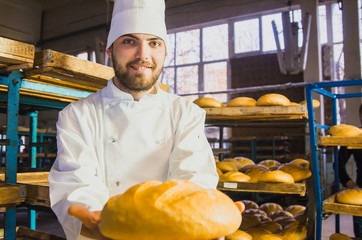 Baker. A young handsome baker working on a bread background holding bread in his hands. Industrial production of bakery products. a man in a special baker's clothes. Bakery