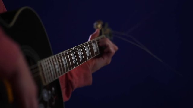 Learning to play chords on acoustic guitar on a blue background closeup