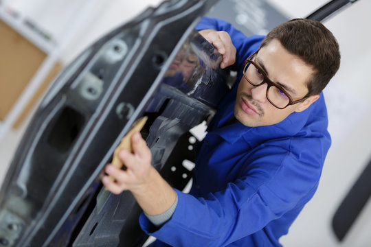 portrait of handsome mechanic in uniform cleaning car door