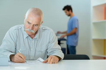 calm senior man writing on paper in library