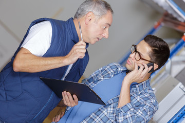 man and co-woker with clipboard and smartphone at warehouse